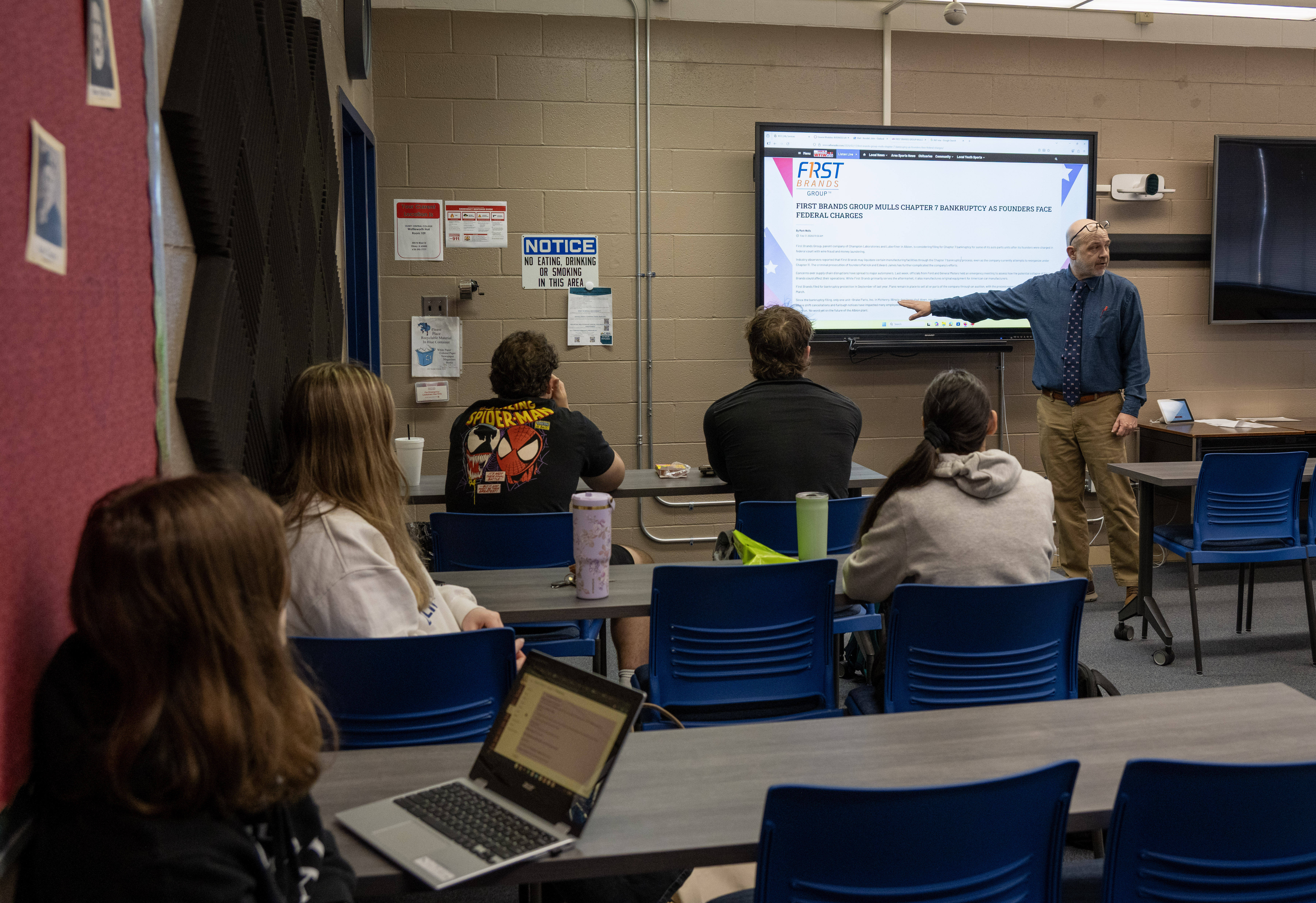Accounting Instructor John Kendall leads a classroom discussion while students view a business news article displayed on a classroom monitor and follow along from their seats.