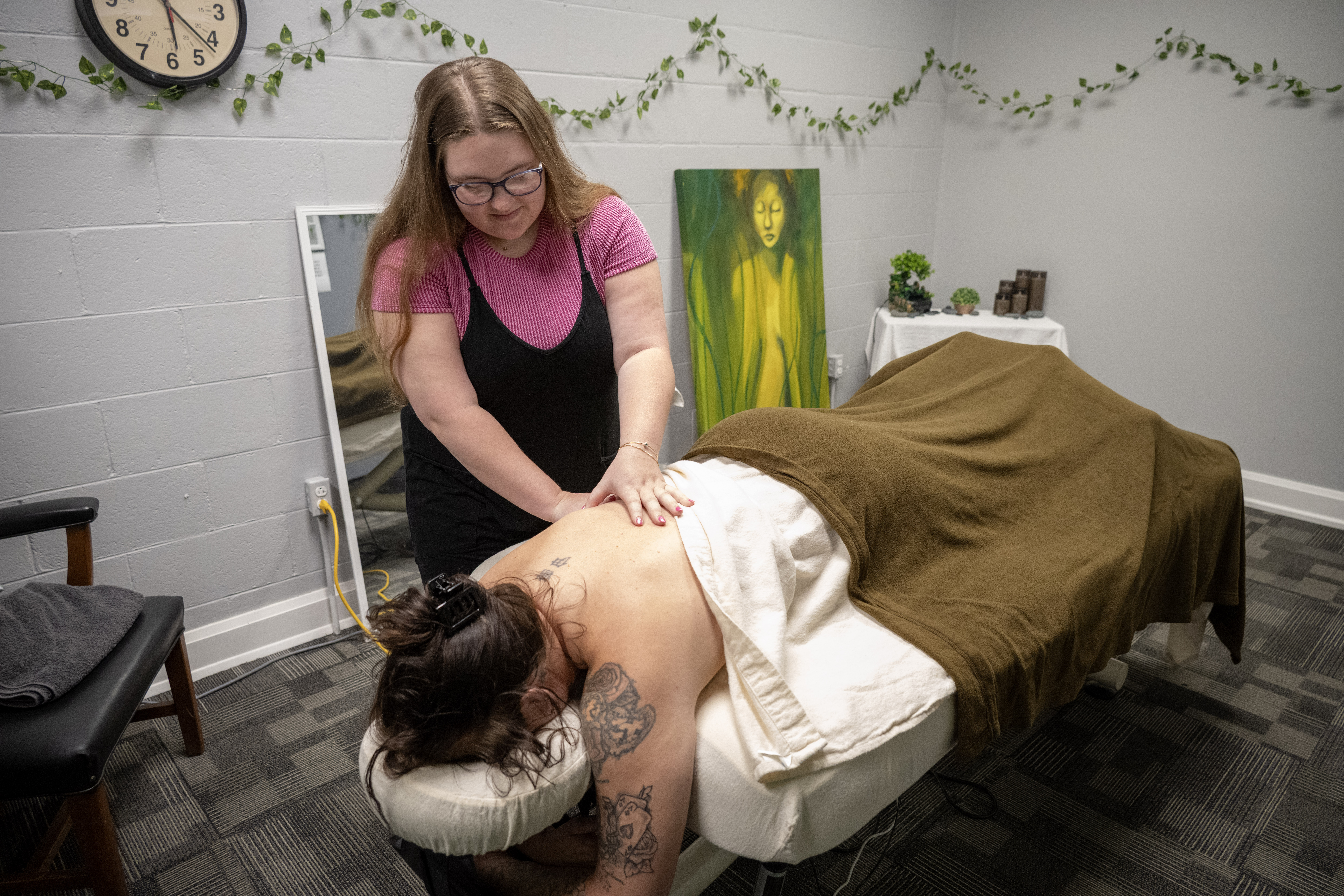 An Olney Central College Massage Therapy student performs a back massage on a client in the program's clinical training space while the client lies face down on a massage table.