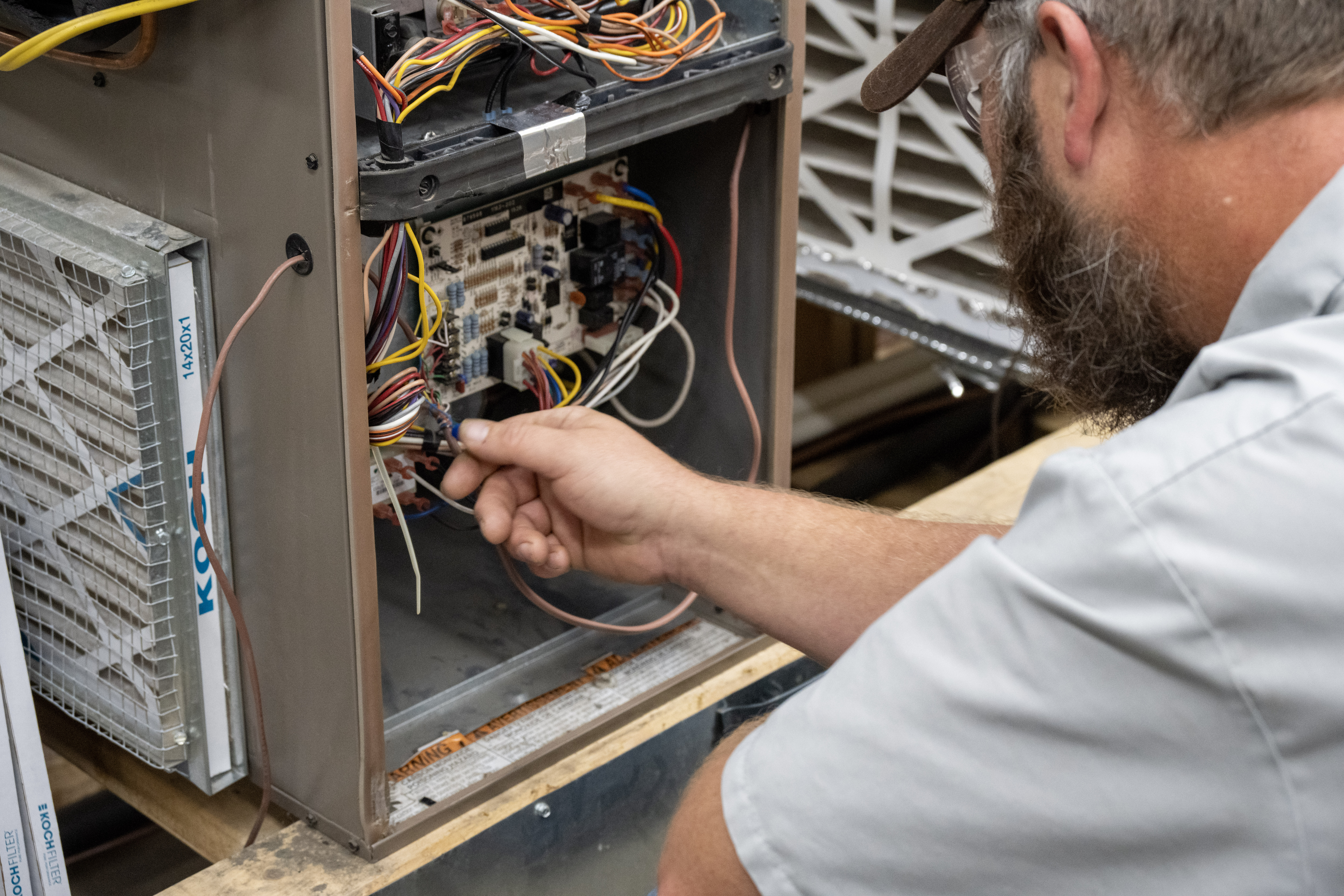 Student troubleshoots wiring inside an HVAC training unit, inspecting electrical components and connections.