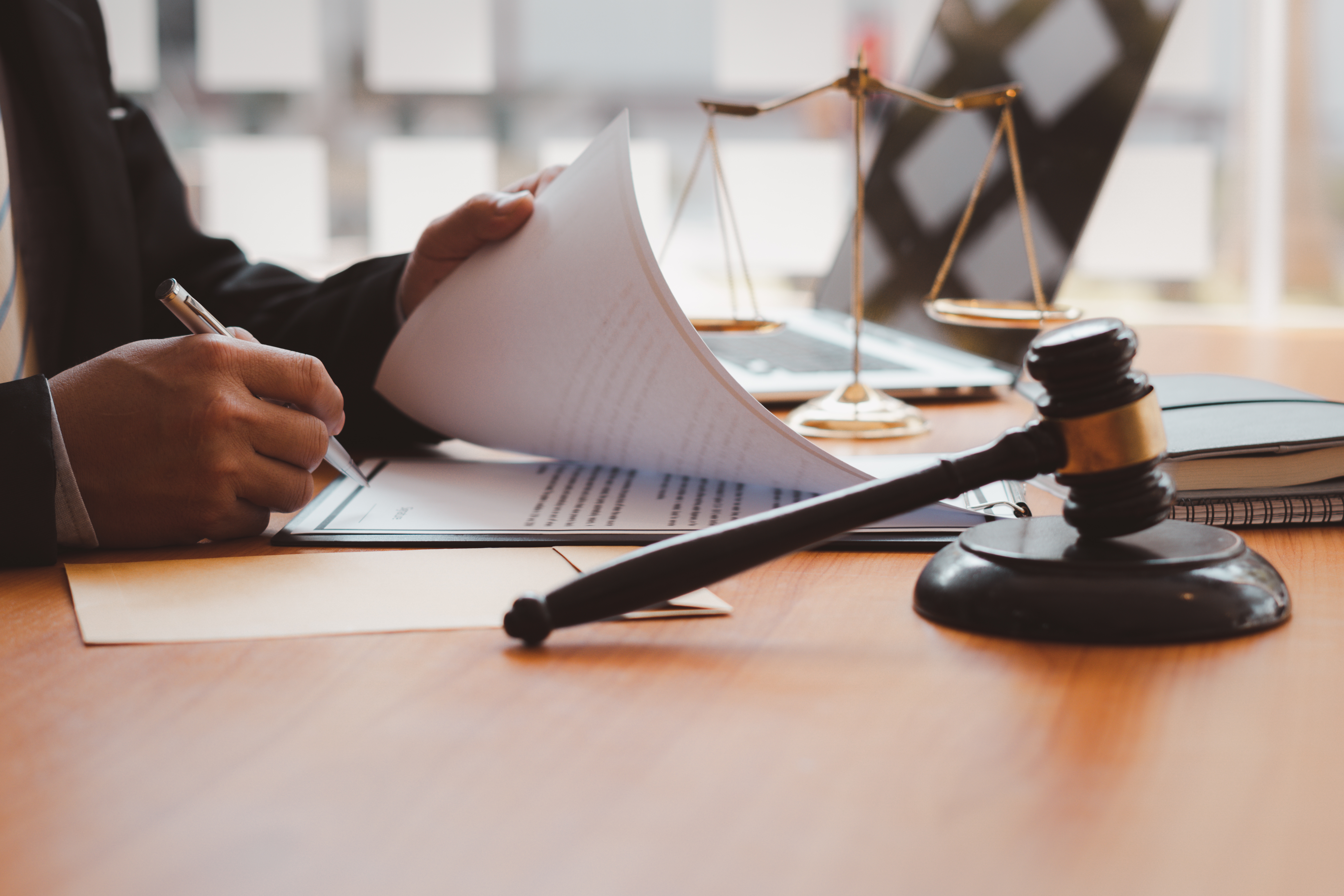 A person reviews and signs legal documents at a desk with a judge’s gavel, scales of justice and law books nearby. The image suggests a political science, pre-law or legal studies theme focused on government, justice, civic systems and the legal process.